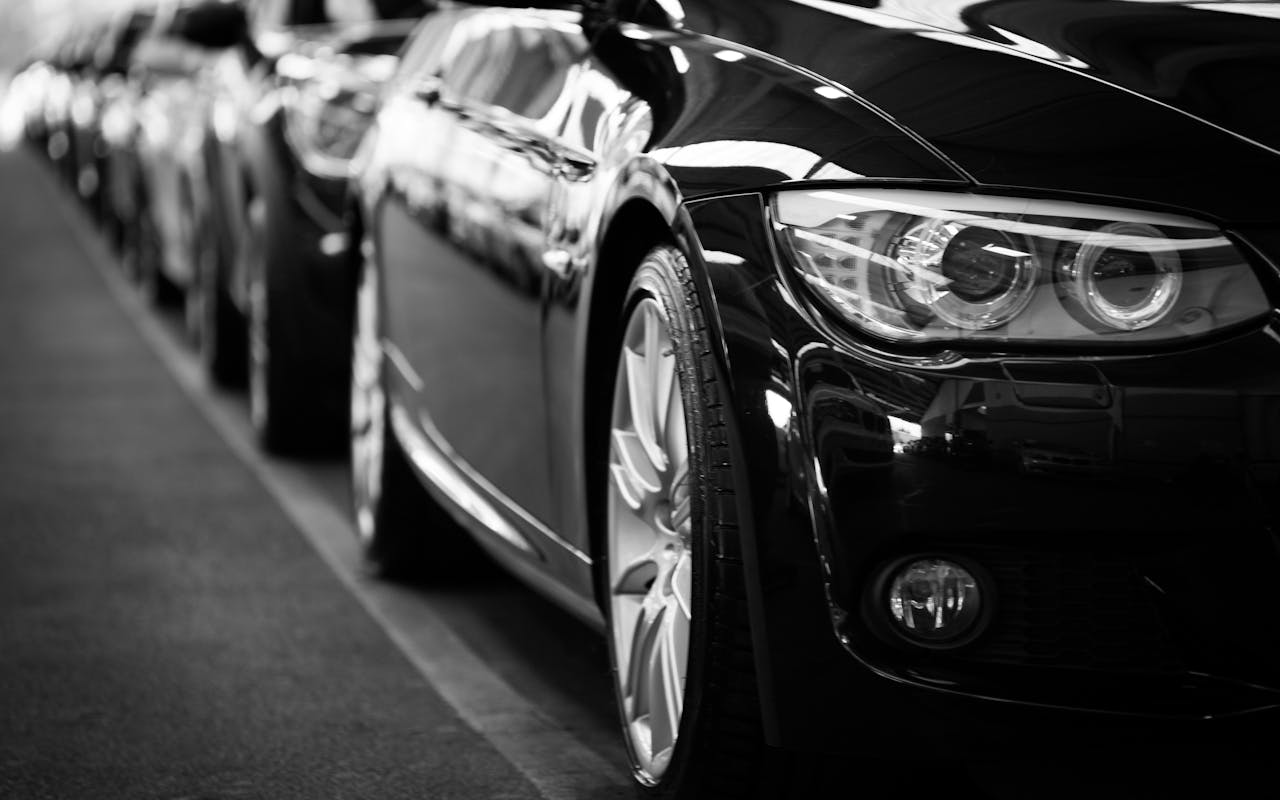 Close-up black and white image of a luxury car line-up focusing on vehicle headlights.